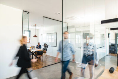 Benefits of flexible working for employers - a blurred photo of three office workers walking through an office - blurred because they are in motion.