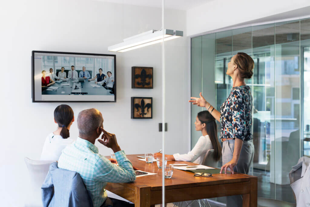 How to run better meetings | CJ. Talent| a group of business people sit in an office looking at a video screen showing their colleagues in a different location.