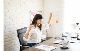 Business woman sits at desk and punches the air in celebration | Best recruitment firms in the uk