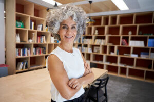 CFO or FD, which is better for your startup - senior businesswoman stands in boardroom/library smiling at camera.